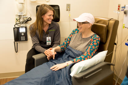 Registered nurse comforting a patient covered with the CapeAble®Care Medical Weighted Blanket during an infusion center treatment session