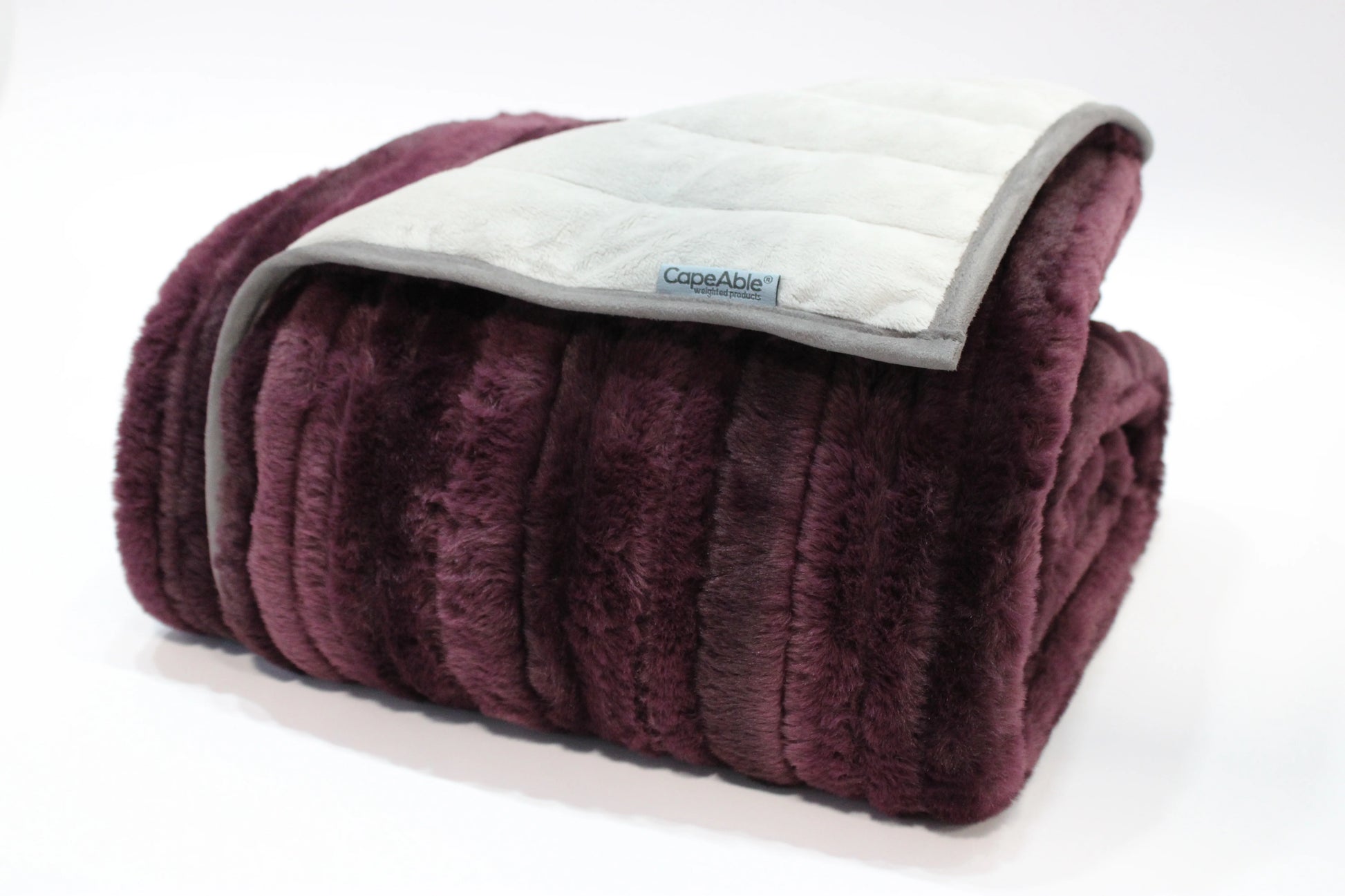 Folded CapeAble weighted blanket with ribbed plum plush exterior and quilted silver-gray interior lining, displayed on white background