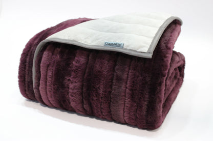 Folded CapeAble weighted blanket with ribbed plum plush exterior and quilted silver-gray interior lining, displayed on white background