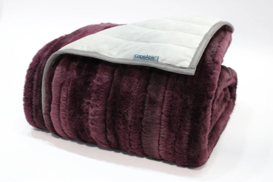 Folded CapeAble weighted blanket with ribbed plum plush exterior and quilted silver-gray interior lining, displayed on white background