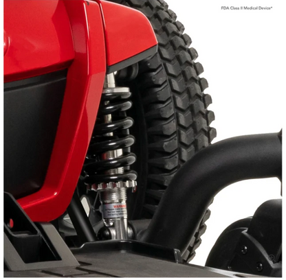 Close-up of an off-road vehicle's rear suspension system, featuring a black coil spring, silver shock absorber, and red body panel next to a black knobby tire.