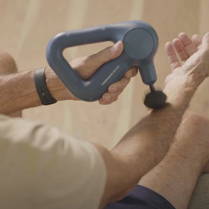 Person using the navy Theragun Relief percussion massage gun on their leg for muscle recovery, tension relief, and relaxation.