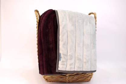 CapeAble weighted blanket draped over a woven basket showing plum ribbed plush exterior and quilted silver-gray interior lining, on white background