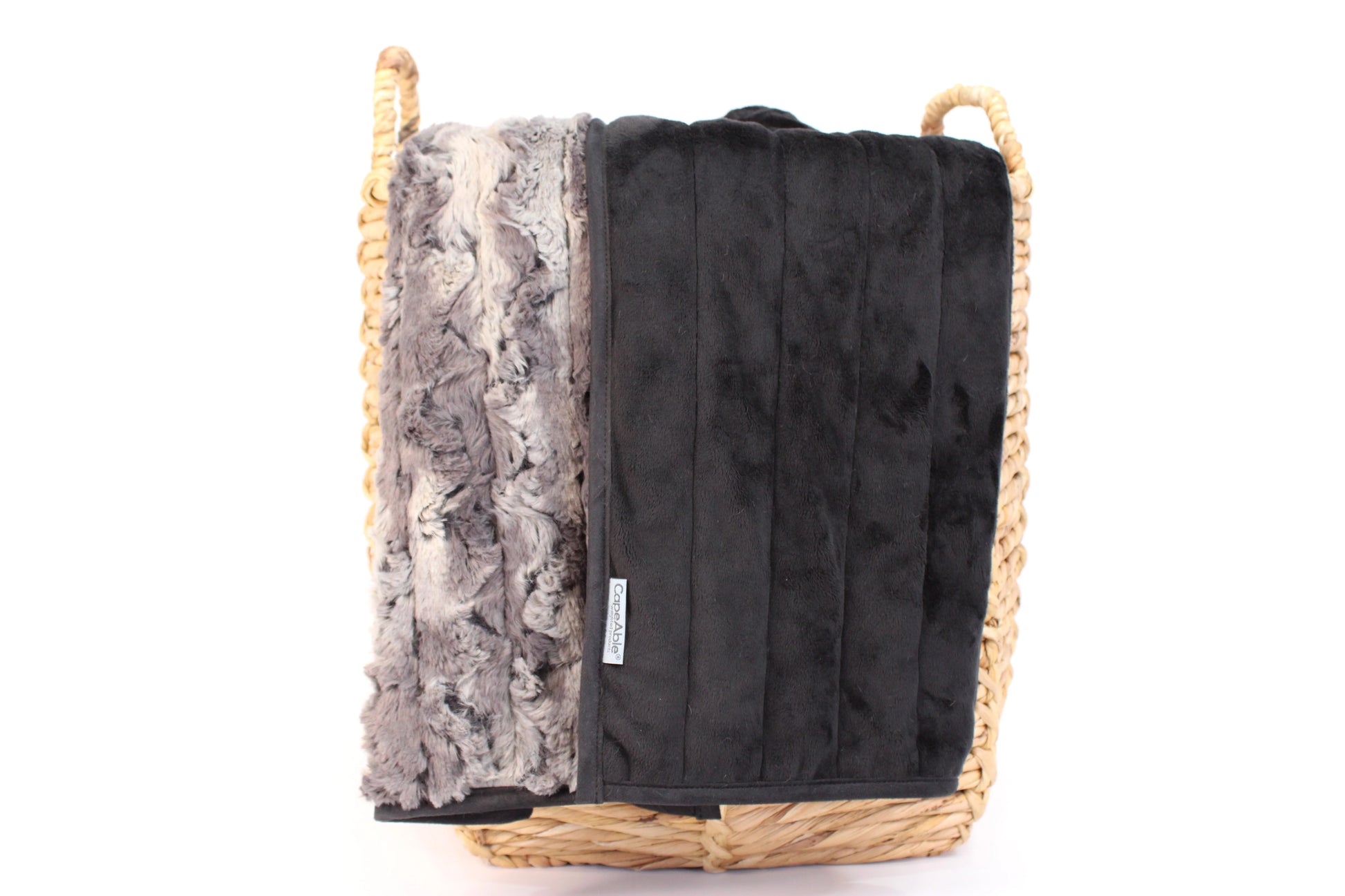 CapeAble weighted blanket in tranquility draped over a woven basket showing gray swirl faux fur exterior and quilted black interior lining, on white background