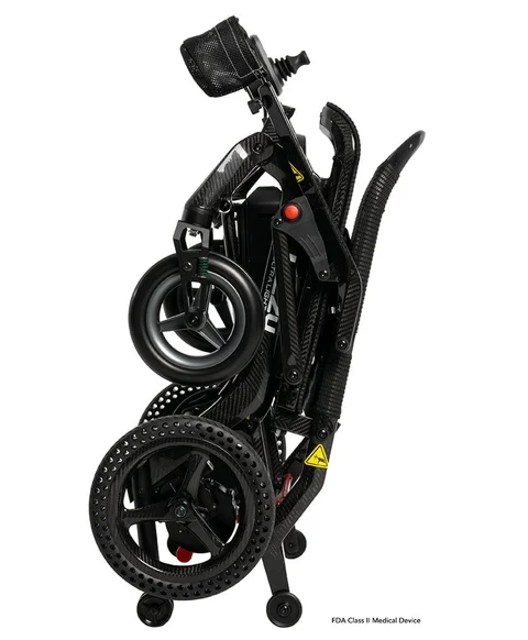 A folded black carbon-fiber electric wheelchair shown on a plain white background, with its large rear wheels, handlebars, and control panel visible.