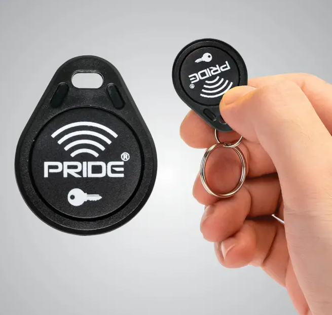 A black RFID key fob and matching key fob reader are shown on a light gray background, with a hand holding the smaller fob attached to a metal key ring.