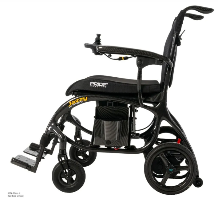 A black electric wheelchair with a carbon fiber frame, shown from a three-quarters side view on a white background. The brand 'Pride Power' is visible on the seat cushion, and 'Jazzy' is on the frame.